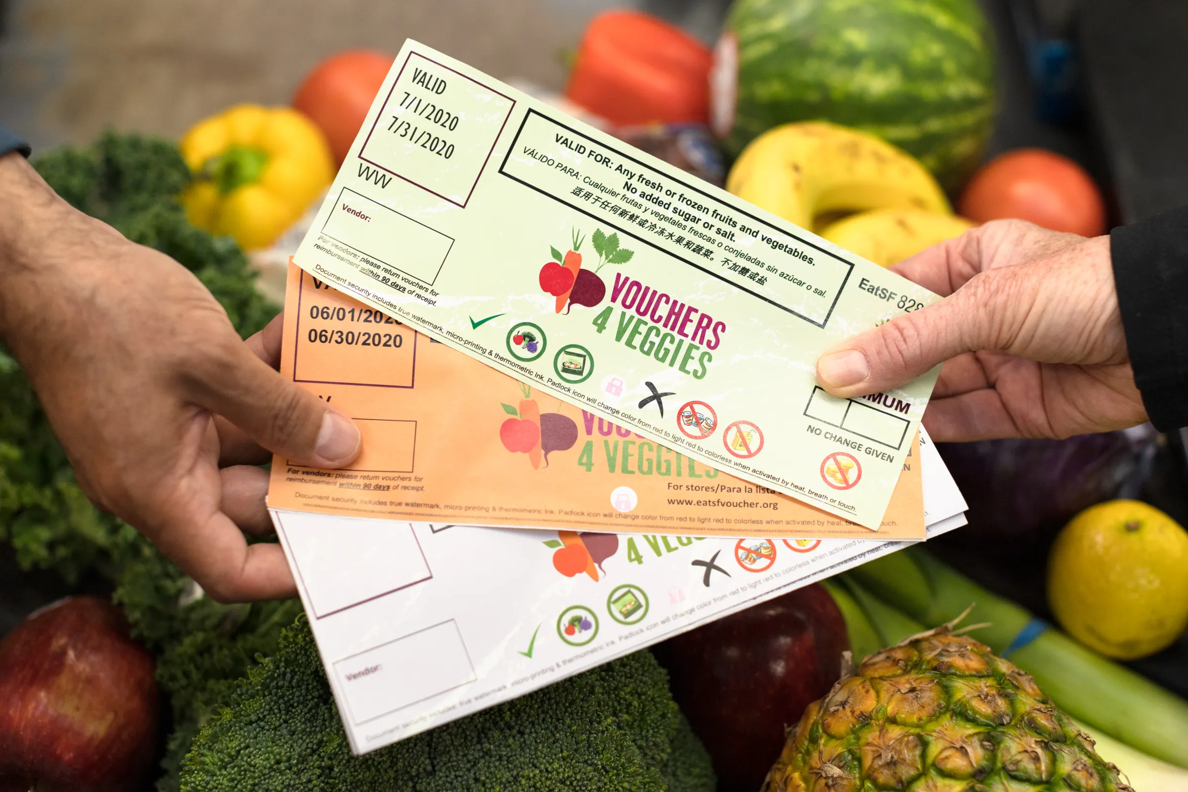 Vouchers 4 Veggies fresh produce vouchers are displayed over a collection of fruits and vegetables.